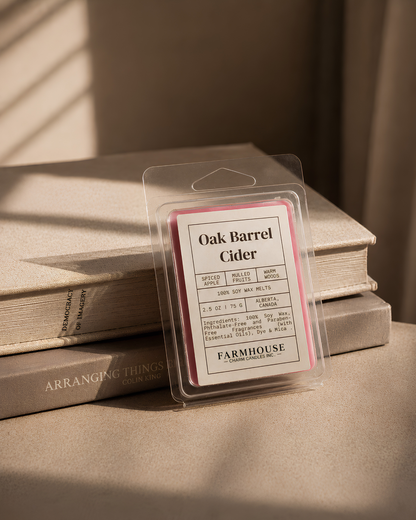 A packaged wax melt labeled 'Oak Barrel Cider' by F Farmhouse Charm Candles, displayed on top of stacked books in warm, sunlit tones.