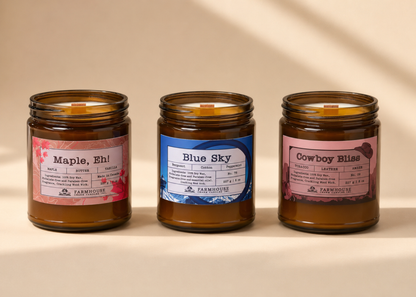 Three jars of candles by Farmhouse Charm Candles with labeled scents (Maple, Eh, Blue Sky and Cowboy Bliss  on a beige background