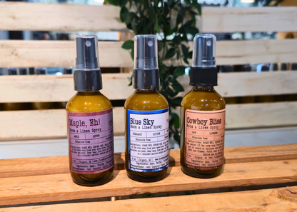 Three small room & linen spray bottles by Farmhouse Charm Candles with labels on a wooden surface.