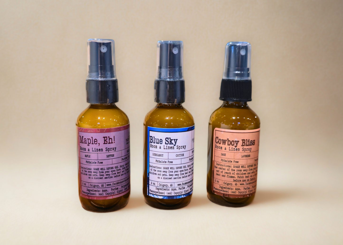 Three small room & linen spray bottles by Farmhouse Charm Candles with labels on a beige background 