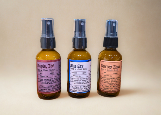 Three small room & linen spray bottles by Farmhouse Charm Candles with labels on a beige background 