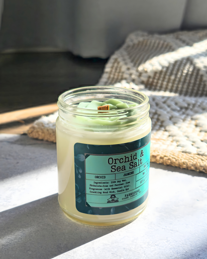 Jar of 'Orchid & Sea Salt' soy candle on a textured surface with a blurred background by Farmhouse Charm Candles