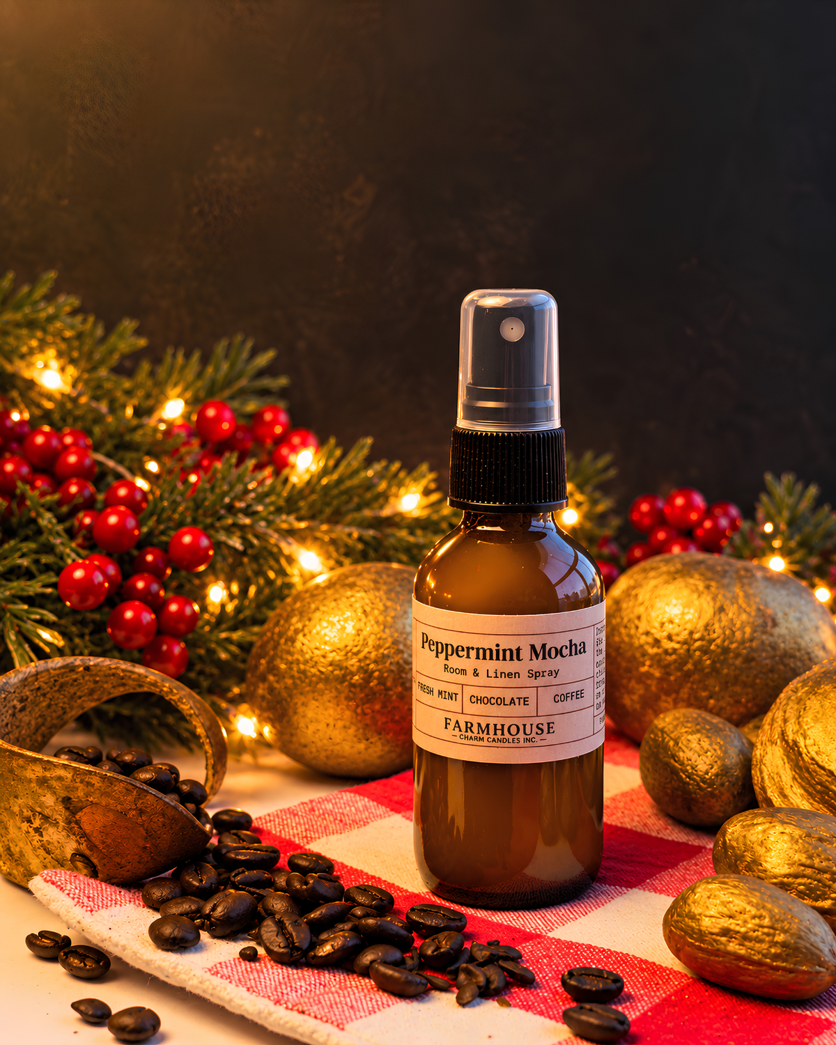 A small amber spray bottle labeled 'Peppermint Mocha' by Farmhouse Charm Candles, styled with coffee beans, gold ornaments, red berries, evergreen branches, and warm string lights on a red-and-white checkered cloth against a dark background.