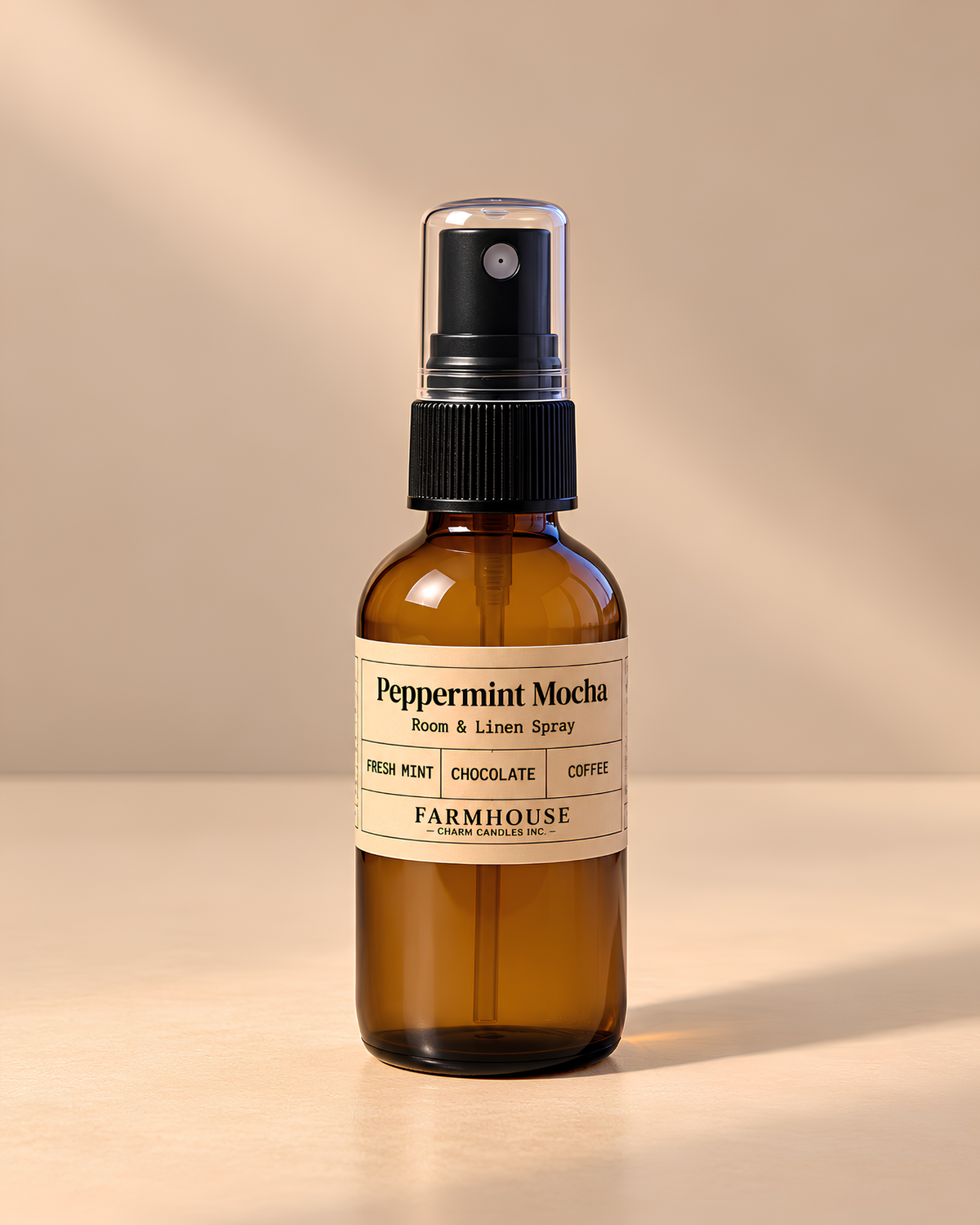 An amber glass room and linen spray bottle with a black spray cap and a cream label reading 'Peppermint Mocha' by Farmhouse Charm Candles set against a warm beige background with soft diagonal shadows.