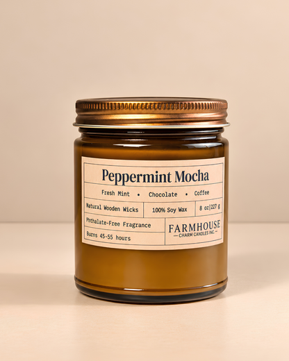 A candle in a brown glass jar with a gold metal lid and a cream-colored label that reads 'Peppermint Mocha' by 'Farmhouse Charm Candles  on a warm beige background.