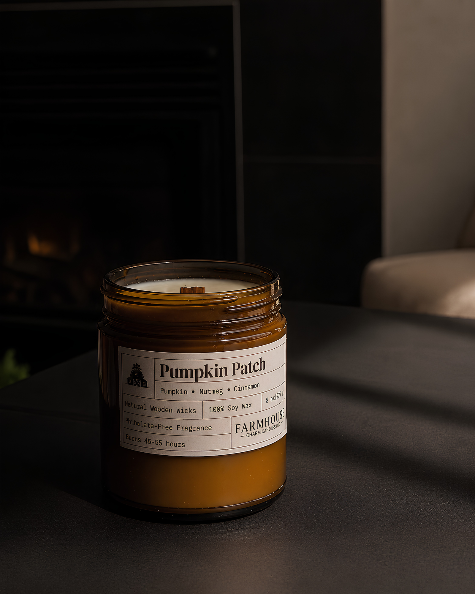 A jar candle labeled 'Pumpkin Patch' by Farmhouse Charm Candles sits on a dark tabletop in a dimly lit indoor setting.