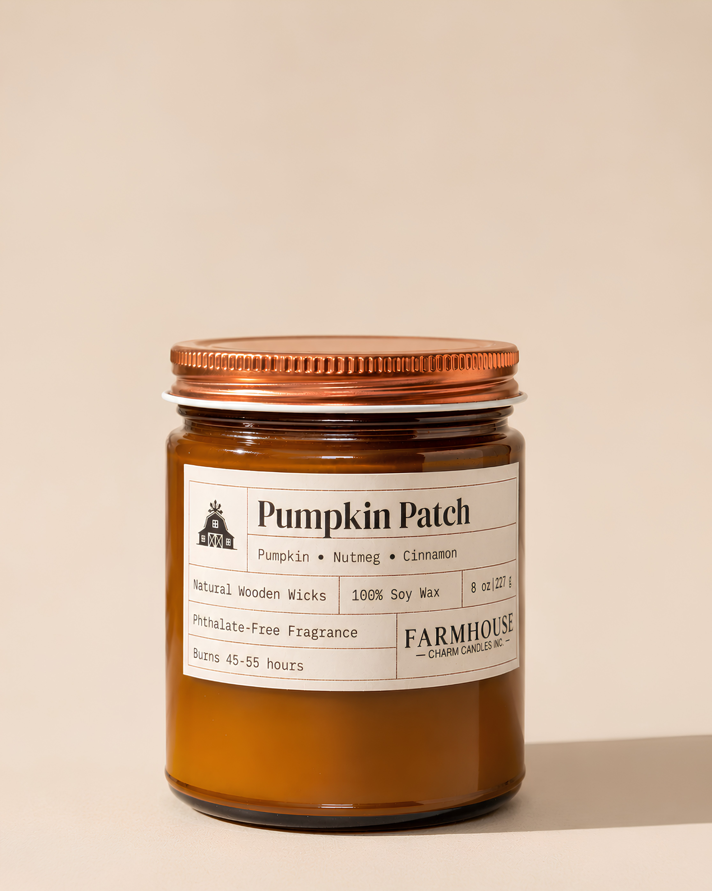 A candle in an amber glass jar with a copper-toned metal lid and a white paper label. The label reads 'Pumpkin Patch' with scent notes of pumpkin, nutmeg, and cinnamon, and shows the brand Farmhouse Charm Candles.