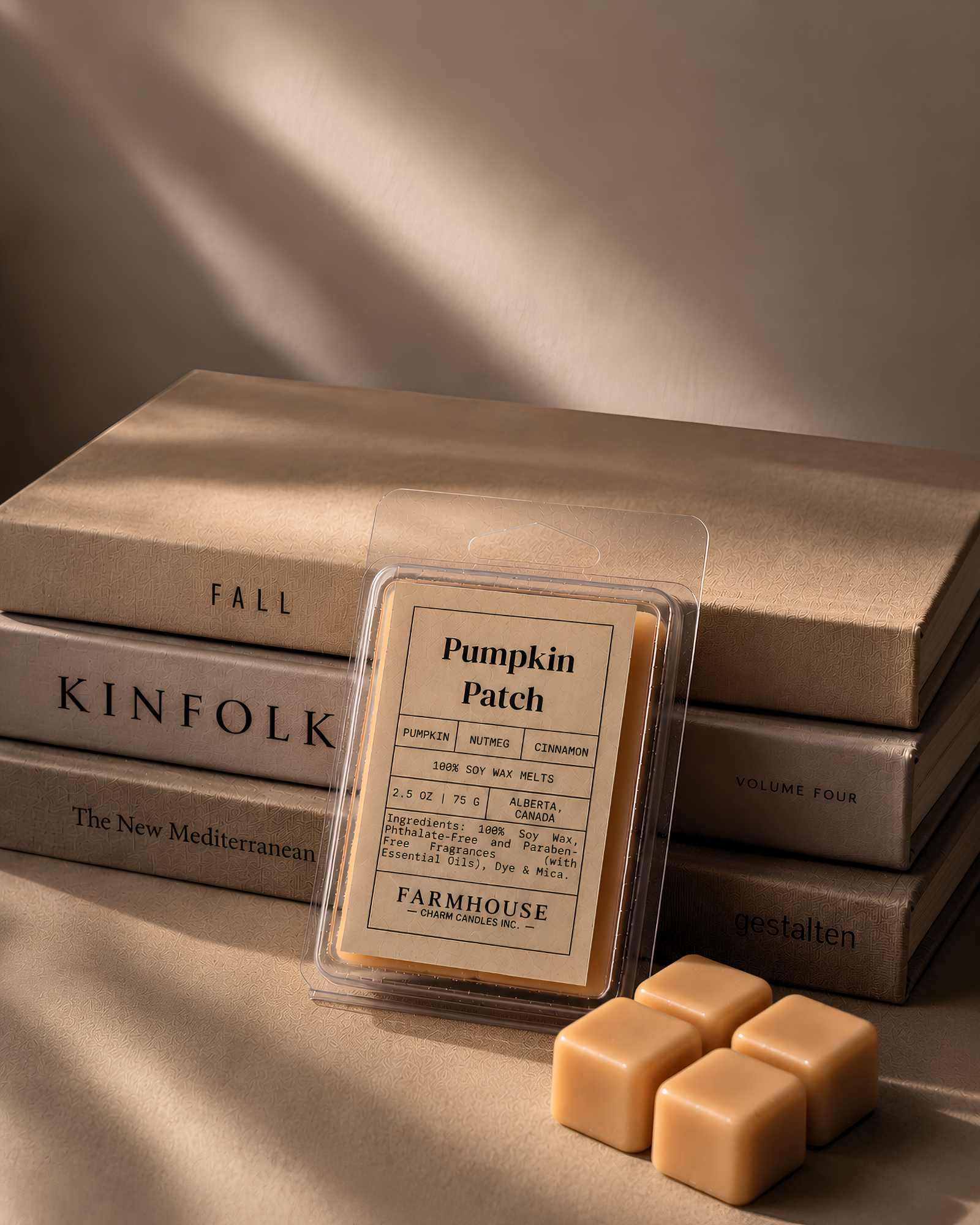 A clear plastic clamshell package labeled 'Pumpkin Patch' by Farmhouse Charm Candles styled in front of stacked beige books with four matching beige wax cubes on a warm beige surface.