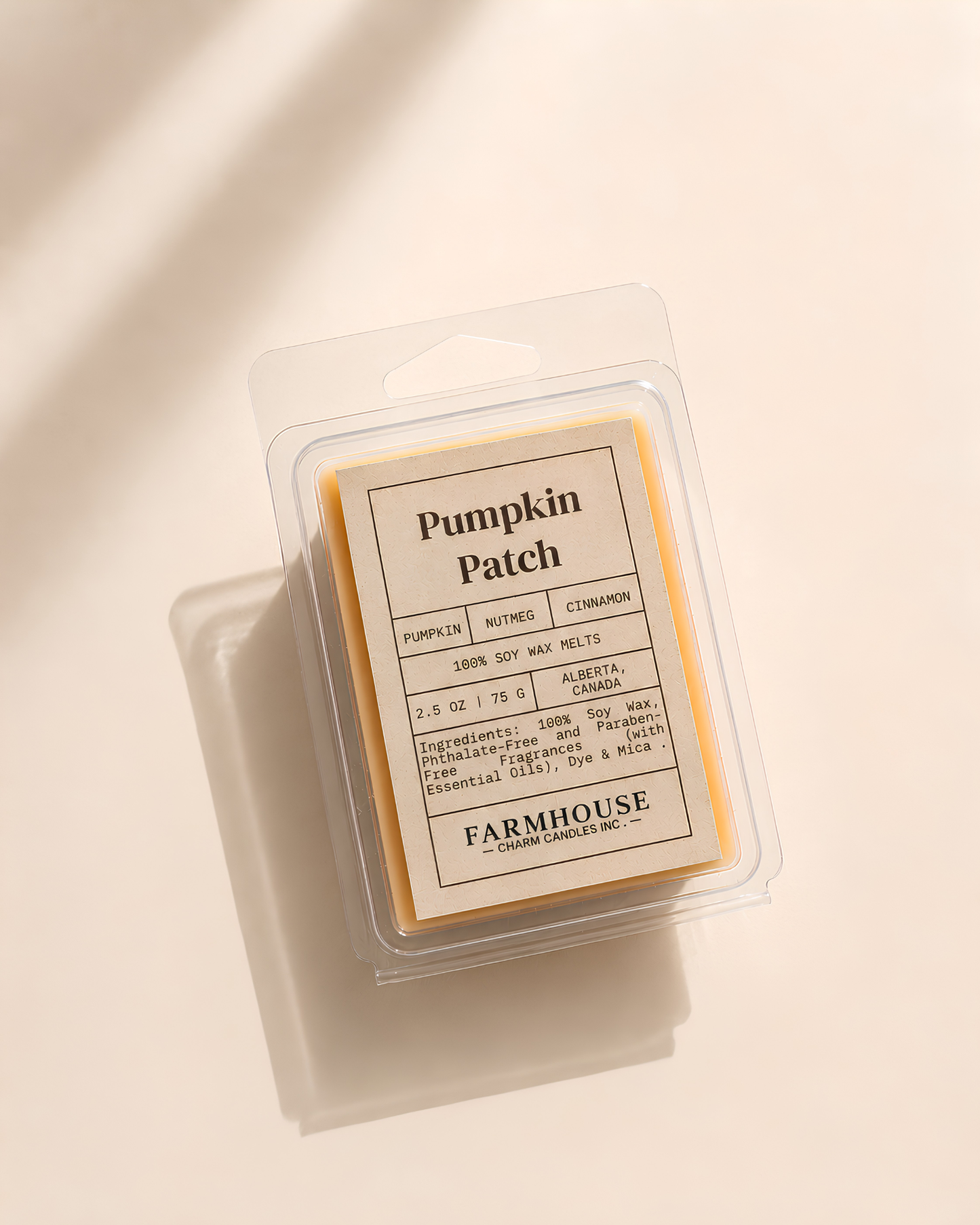 A packaged pumpkin patch scented wax melt from Farmhouse Charm Candles, shown in a clear clamshell container with a cream-colored label and yellow wax visible inside, photographed on a warm off-white background with soft diagonal shadows.