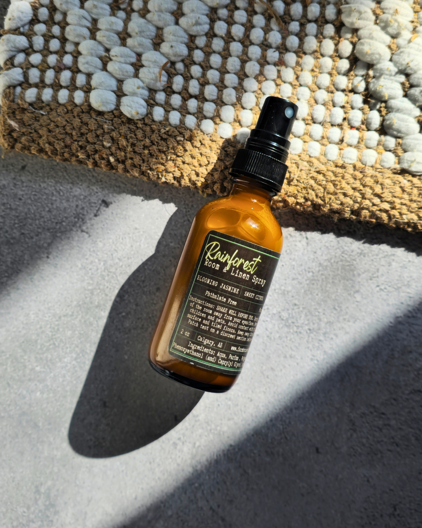 Brown bottle  of Rainforest Room & Linen Spray by Farmhouse charm candles with black cap on a textured surface