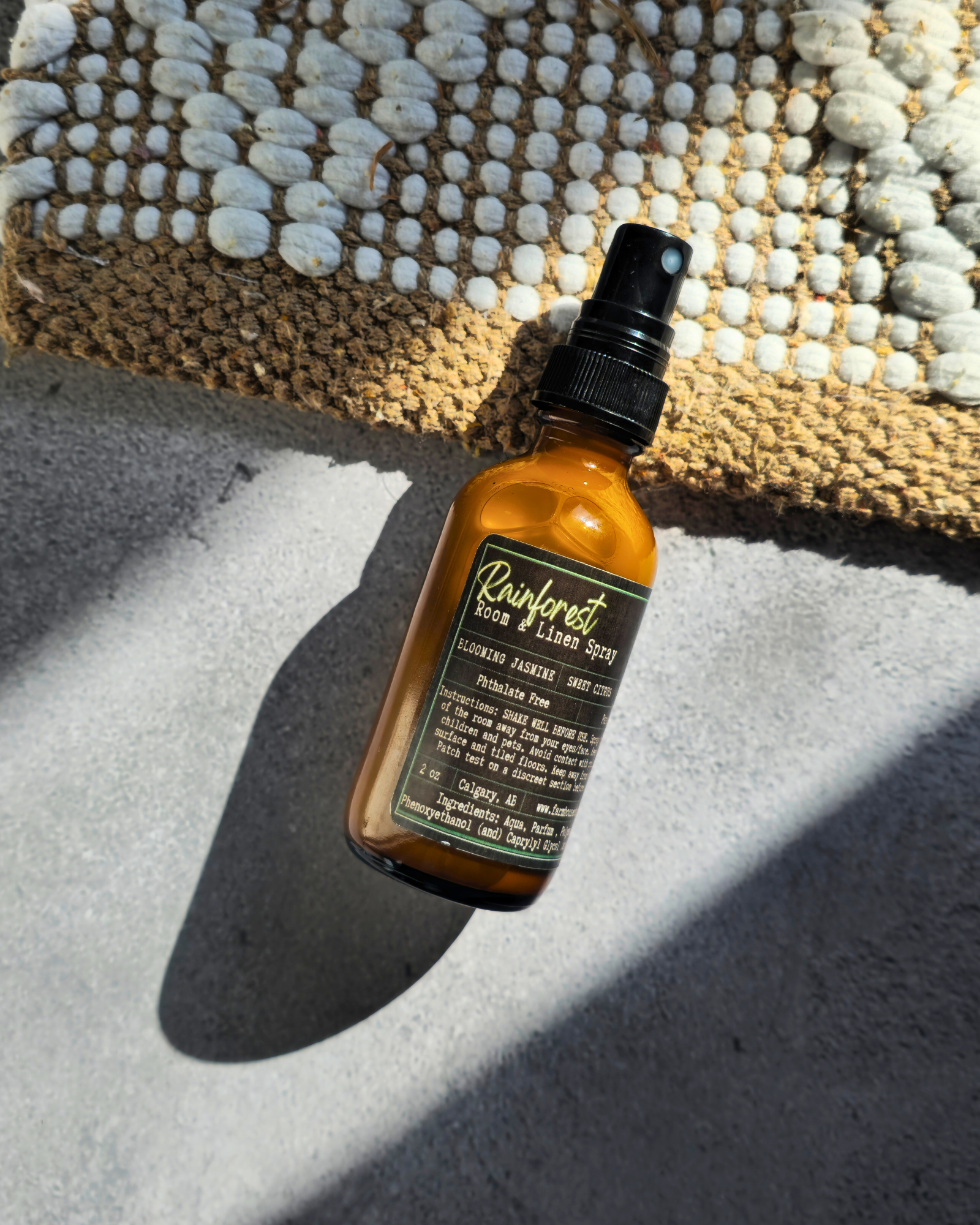 Brown bottle  of Rainforest Room & Linen Spray by Farmhouse charm candles with black cap on a textured surface
