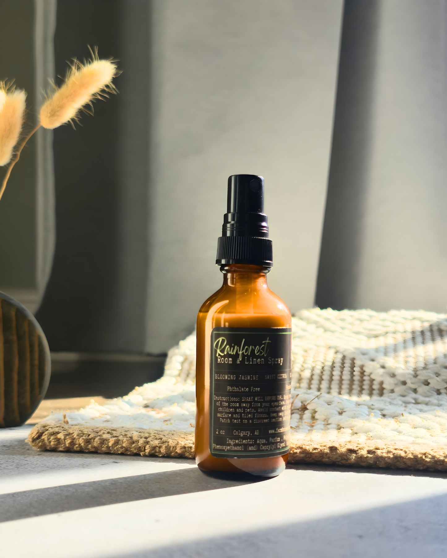 Amber bottle of room & linen spray  with Rainforest label by Farmhouse Charm Candles on a textured surface with light and shadow