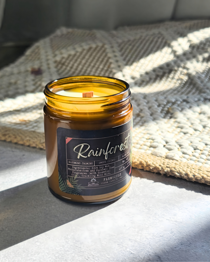 Candle in a glass jar labeled 'Rainforest by Farmhouse Charm Candles on a textured surface
