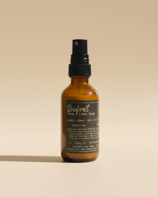 Amber room & linen spray bottle with Rainforest label by Farmhouse Charm Candles on a textured surface