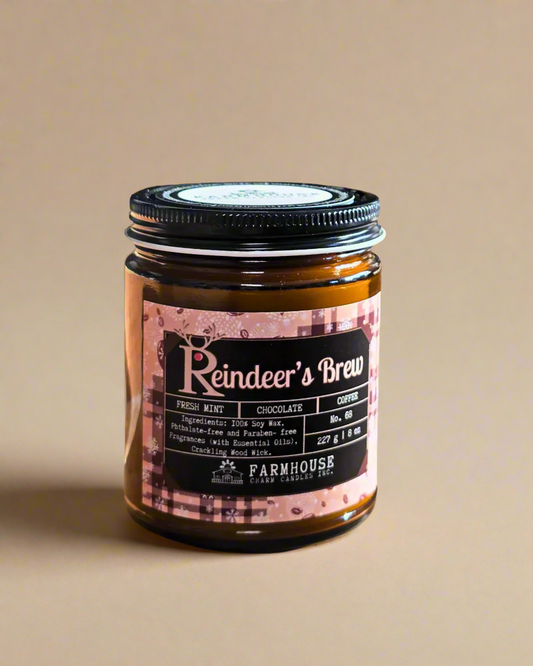 Reindeer’s Brew soy candle in amber jar with warm holiday glow, surrounded by coffee beans, peppermint, and chocolate pieces — cozy Christmas scent from Farmhouse Charm Candles.