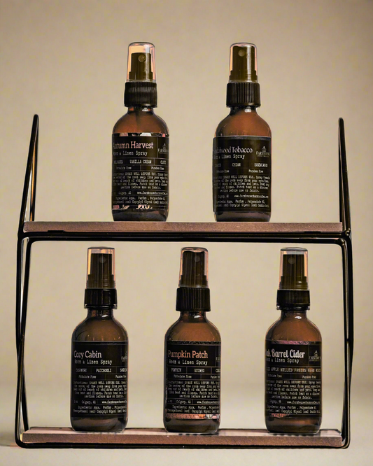 Set of five brown room & linen spray bottles by Farmhouse Charm Candles with labels on a wooden shelf against a beige background