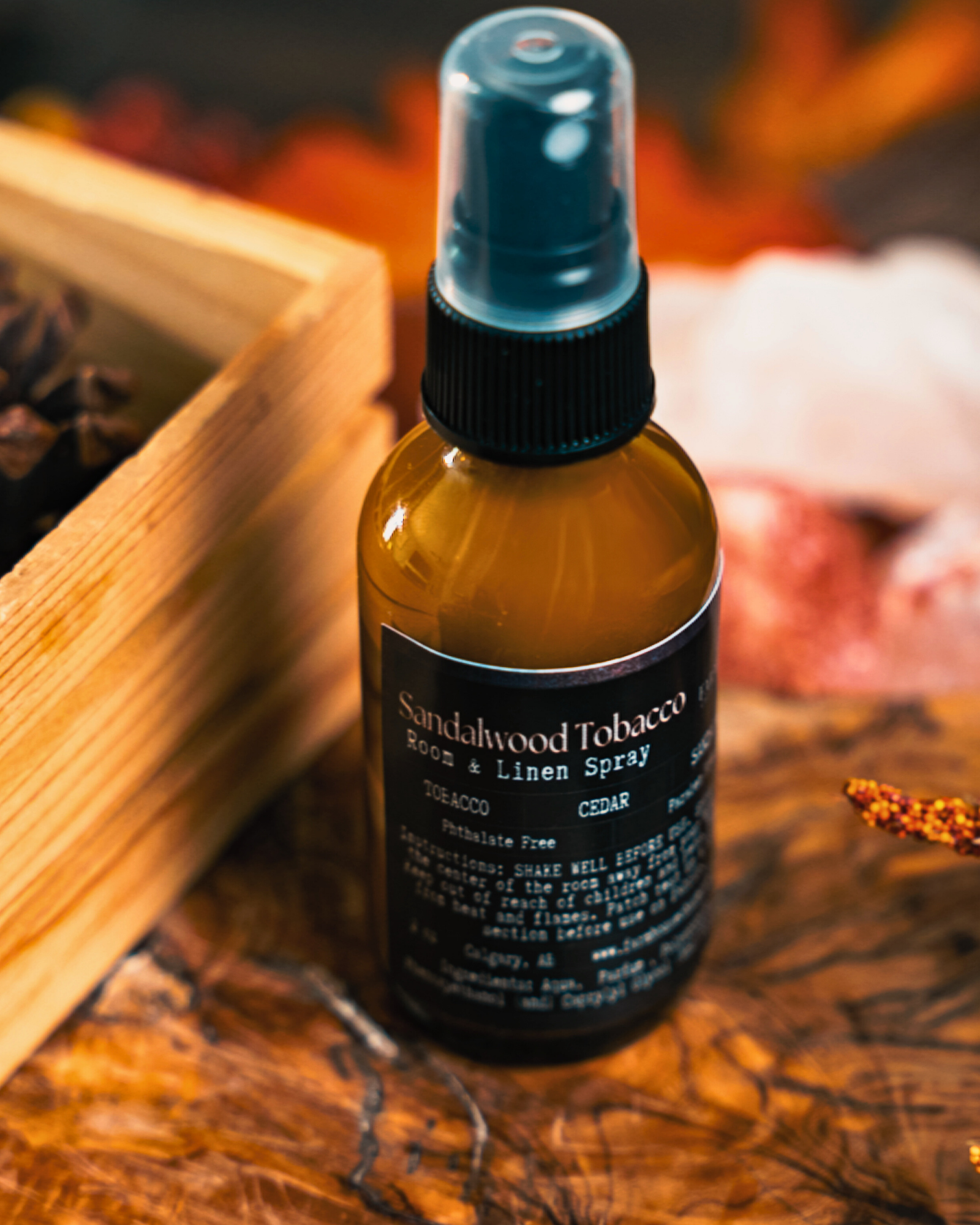 Bottle of Sandalwood Tobacco Room & Linen Spray by Farmhouse Charm Candles on a wooden surface