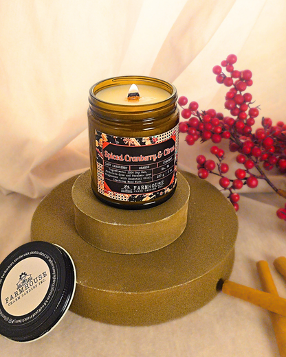 Spiced Cranberry & Citrus soy candle by Farmhouse Charm Candle in amber jar surrounded by fresh cranberries and cinnamon sticks — a cozy holiday scent that blends tart, sweet, and warm notes.
