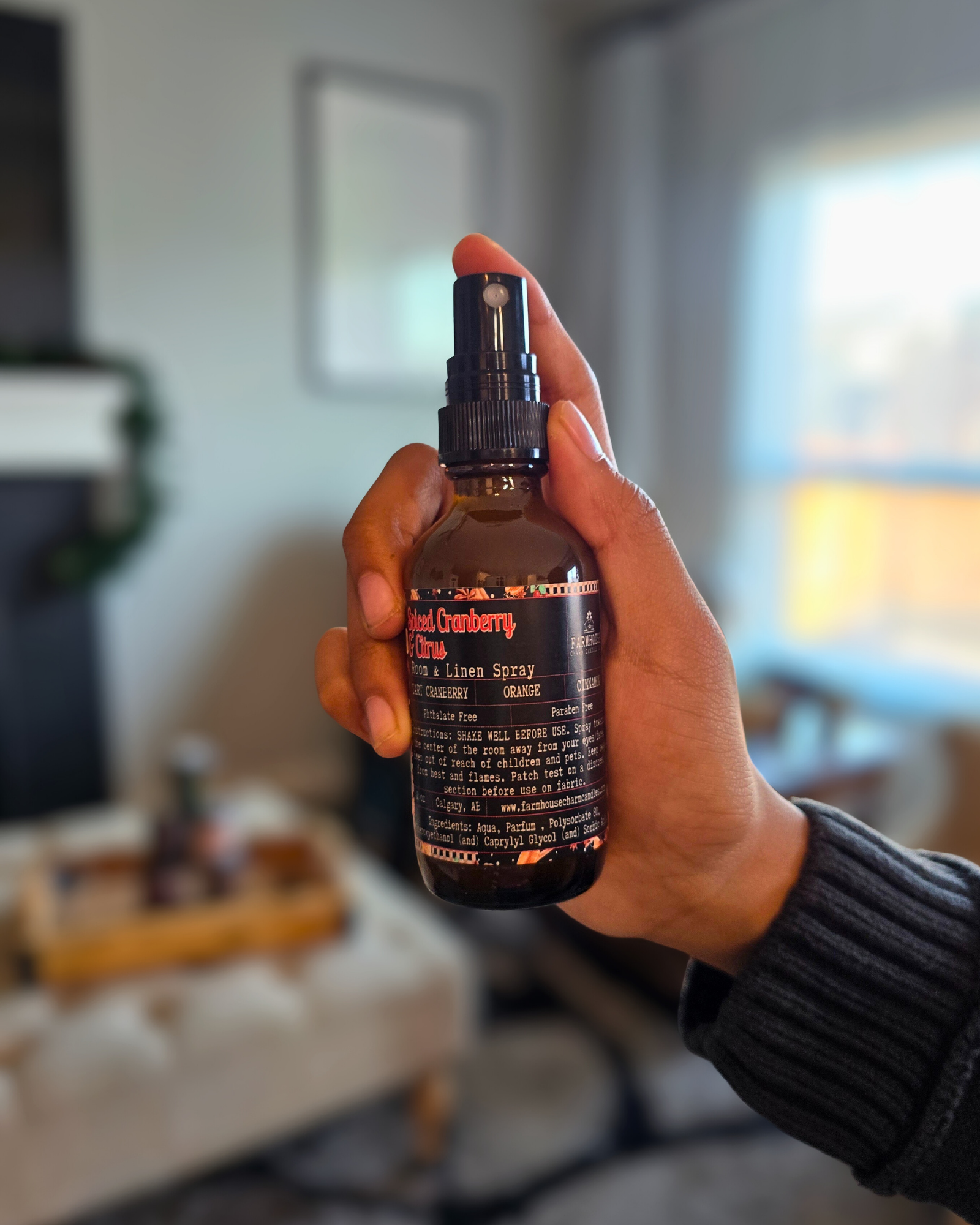 Hand holding an amber glass bottle of Spiced Cranberry & Citrus Room and Linen Spray — evokes a warm, cozy Christmas scent of cranberry, orange, and cinnamon.