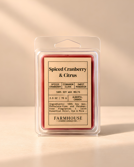 A packaged wax melt product labeled 'Spiced Cranberry & Citrus' by Farmhouse Charm Candles in a clear plastic clamshell package on a warm beige background. The wax melts inside have a red-orange border and a cream center label with black text.