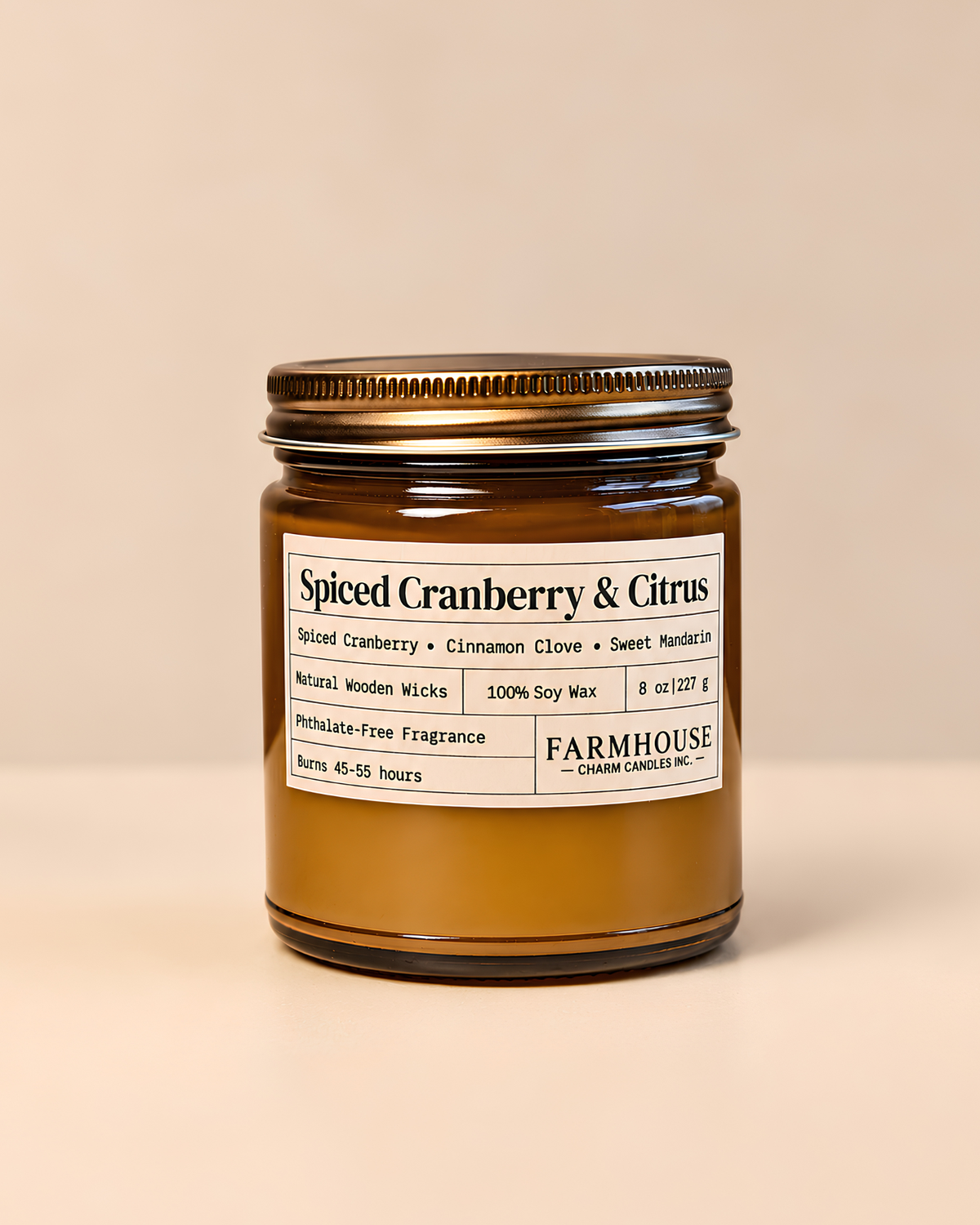 A Farmhouse Charm Candles  'Spiced Cranberry & Citrus' soy wax candle in an amber glass jar with a gold metal lid, set against a solid beige background.