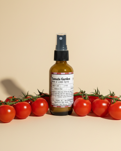 Bottle of Tomato Garden Room & Linen Spray by Farmhouse Charm Candles surrounded by cherry tomatoes on a beige background