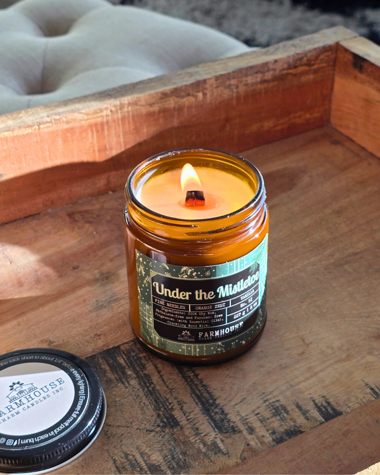 Candle in a glass jar with a label Under the Mistletoe by Farmhouse Charm Candles on a wooden surface