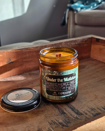 Candle in a glass jar with a label under the mistletoe by Farmhouse Charm Candles on a wooden surface