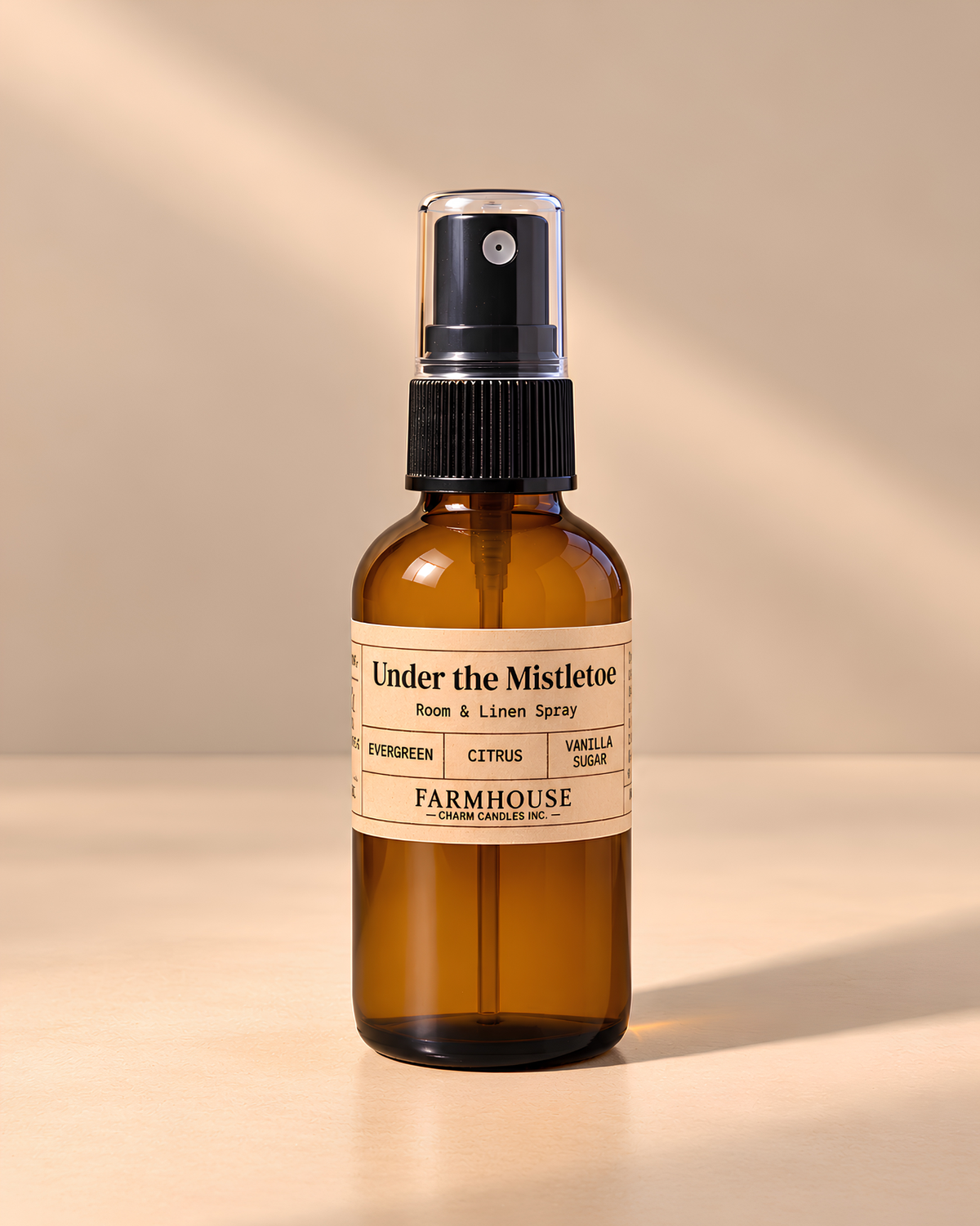 An amber glass room and linen spray bottle with a black spray cap and a cream label reading 'Under the Mistletoe' by 'FARMHOUSE Charm Candles', photographed on a warm beige background with soft diagonal light rays.