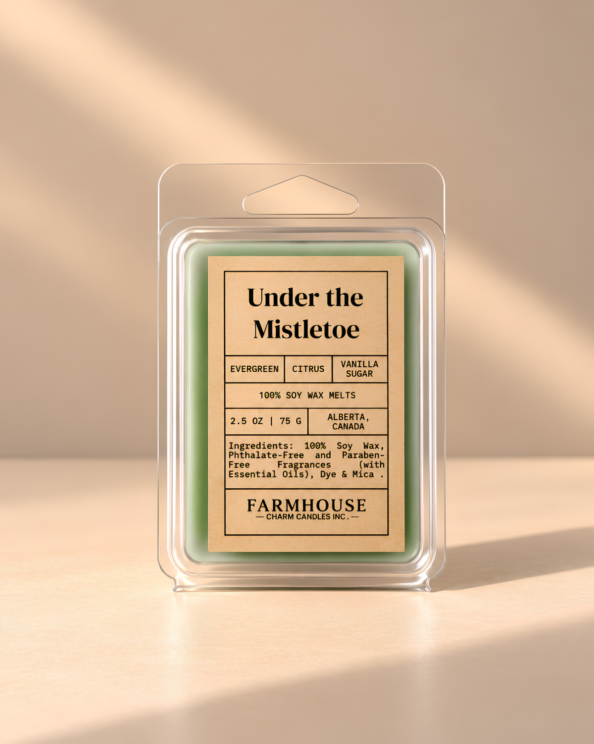 A packaged soy wax melt in a clear plastic clamshell package with a beige label reading 'Under the Mistletoe' by Farmhouse Charm Candles on a warm beige background with soft sunlight and shadows.