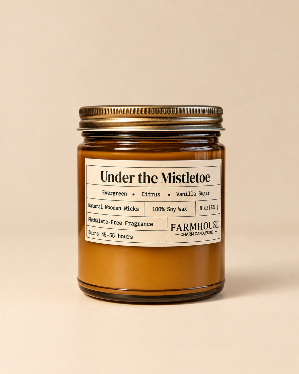 An amber glass jar candle with a gold metal lid and a cream-colored label reading 'Under the Mistletoe' by Farmhouse  Charm Candle, set against a solid beige background.