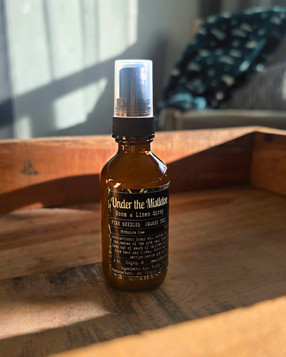 Brown spray bottle with label ' Under the Mistletoe by Farmhouse charm Candles on a wooden surface