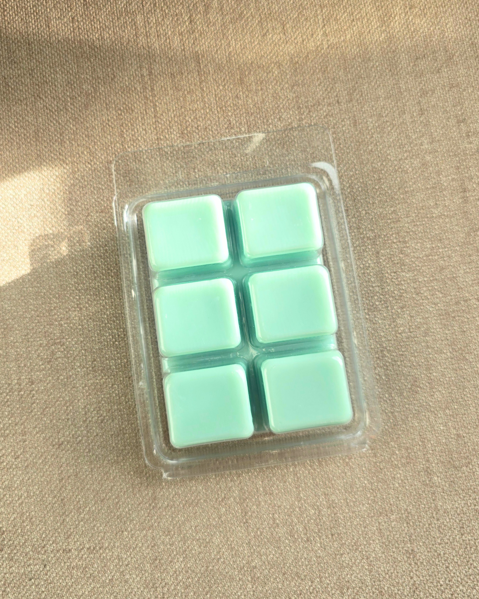 Pack of six light green cubes in clear plastic packaging  of wax melts on a beige surface by Farmhouse Charm Candles